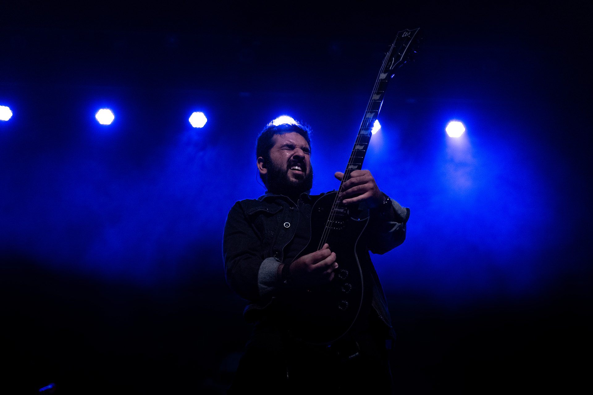 Filipe Hanssen no palco, com a guitarra sob luzes azuis.